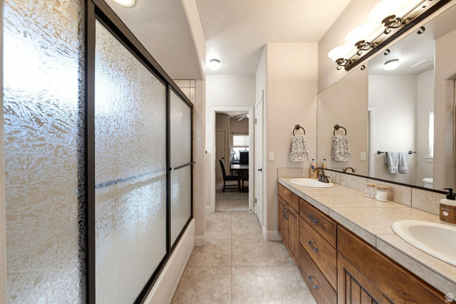 1609 East 10 S Street St. George, UT 84790 - Photo 37 of 68 Dual vanity with wood-finish cabinetry and tile countertops, complemented by a large mirror and multi-bulb sconce lighting