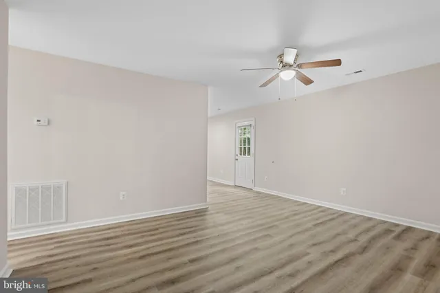 an empty room with wooden floor ceiling fan and windows