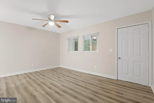 a view of an empty room with wooden floor and a ceiling fan