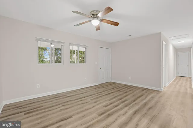 an empty room with wooden floor ceiling fan and windows