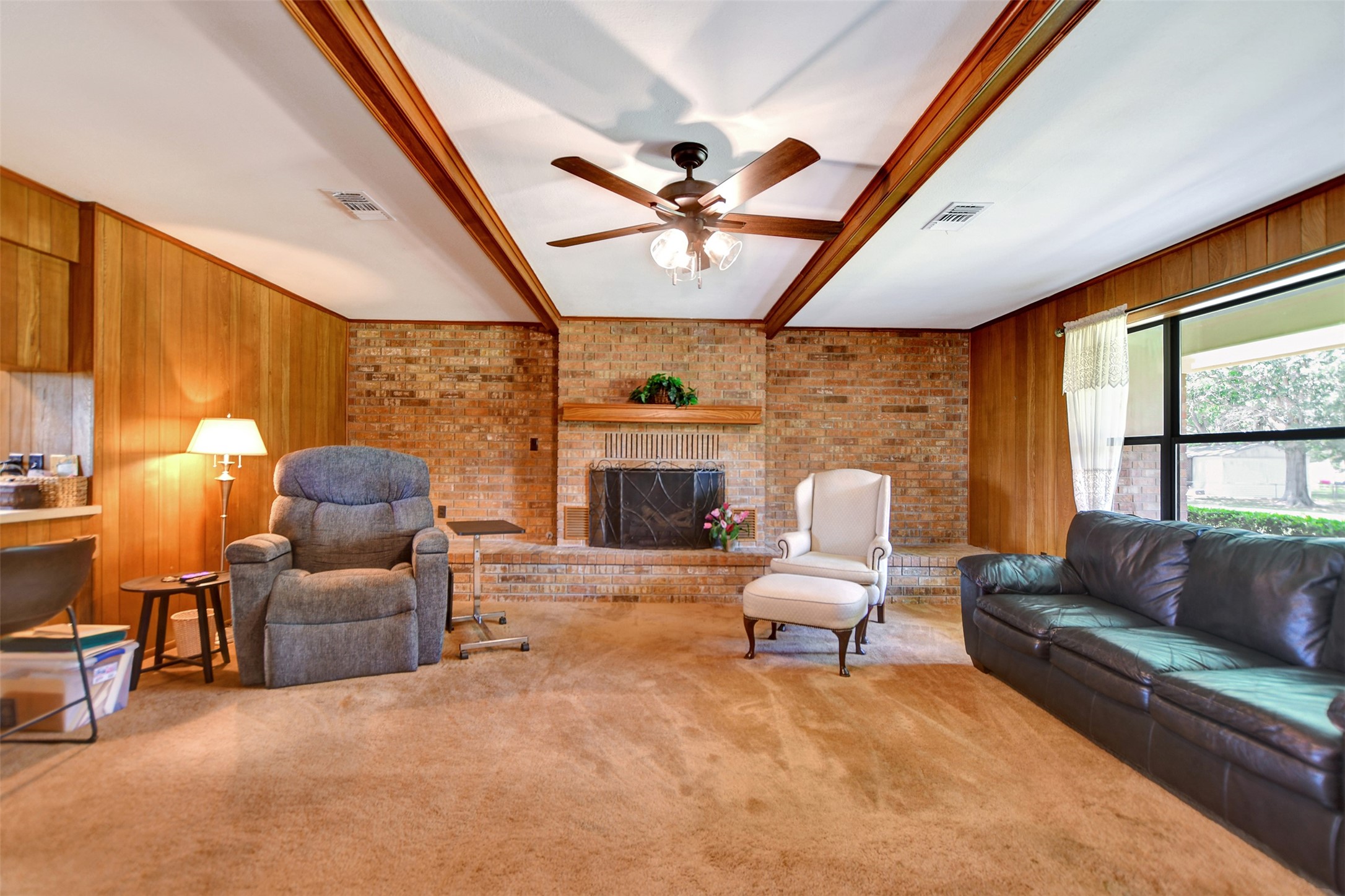 341 South S Loop Bellville, TX 77418 - Photo 7 of 33 Cozy living room with wood paneling, featuring a brick fireplace, ceiling fan, and large window for natural light.