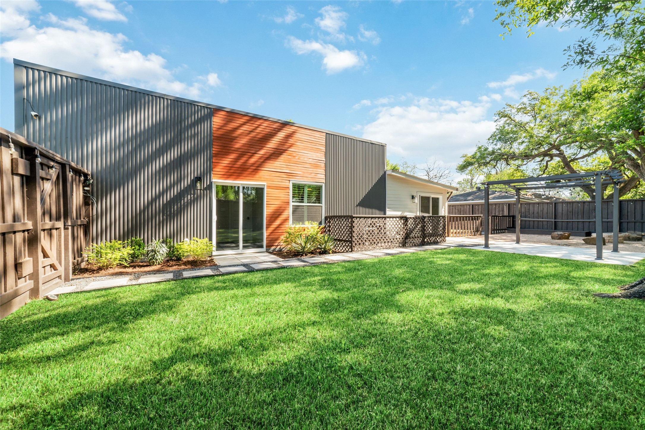 9400 Spring Branch Drive Houston, TX 77080 - Photo 3 of 45 Modern backyard featuring a sleek, contemporary facade with a mix of metal and wood accents, lush green lawn, and a spacious patio area perfect for outdoor entertaining.
