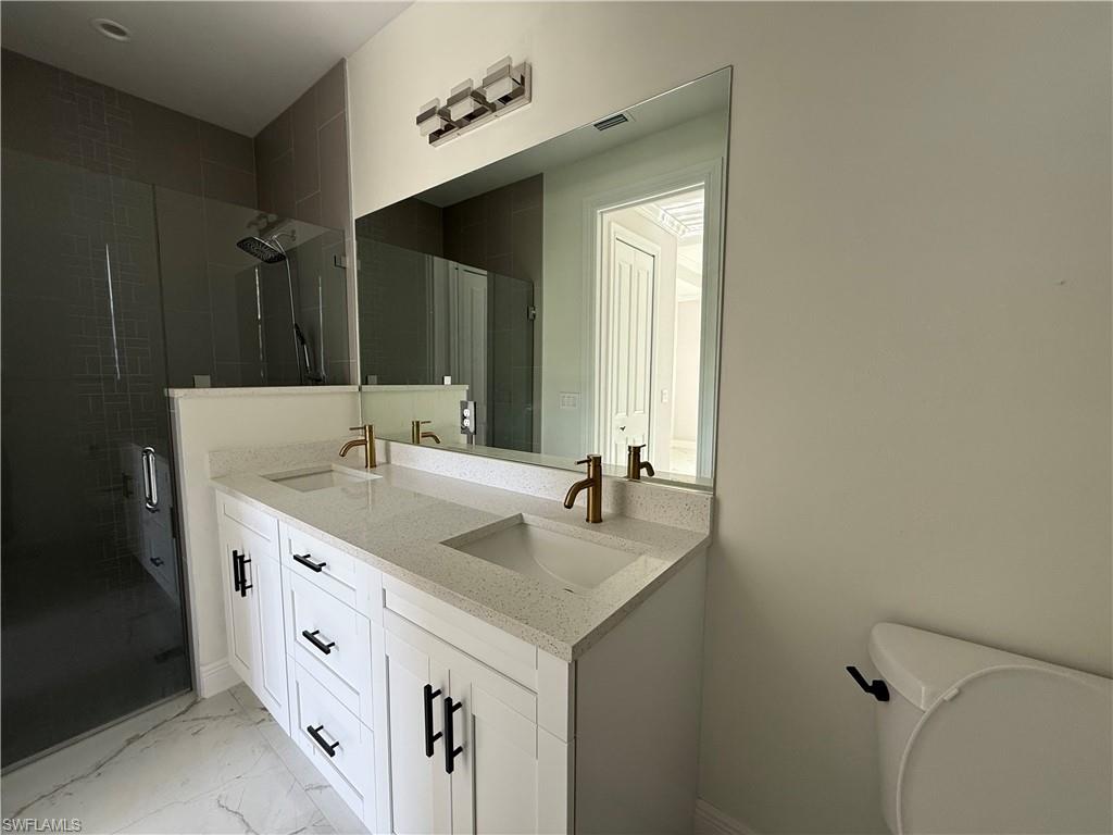 4768 40th Street Northeast Naples, FL 34120 - Photo 13 of 18 Dual vanity featuring white cabinetry, bronze-finish fixtures, and a white flecked countertop