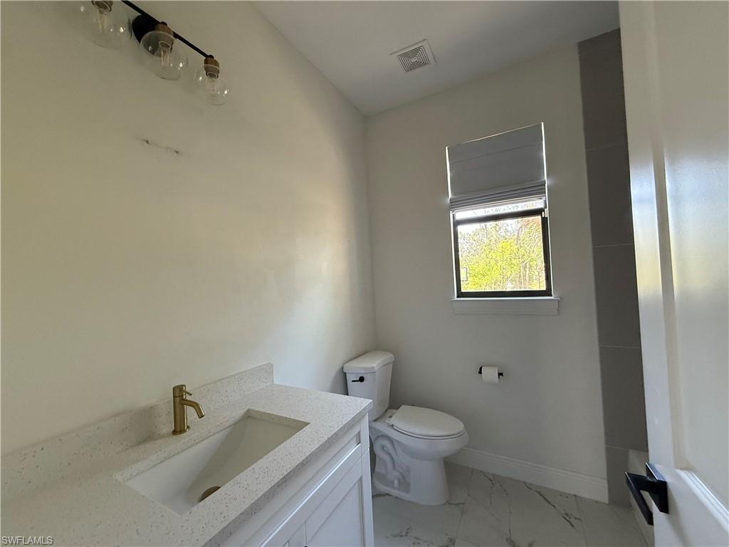 4768 40th Street Northeast Naples, FL 34120 - Photo 15 of 18 Modern bathroom featuring a white vanity with an integrated rectangular sink, speckled countertop, and a brass-finish faucet