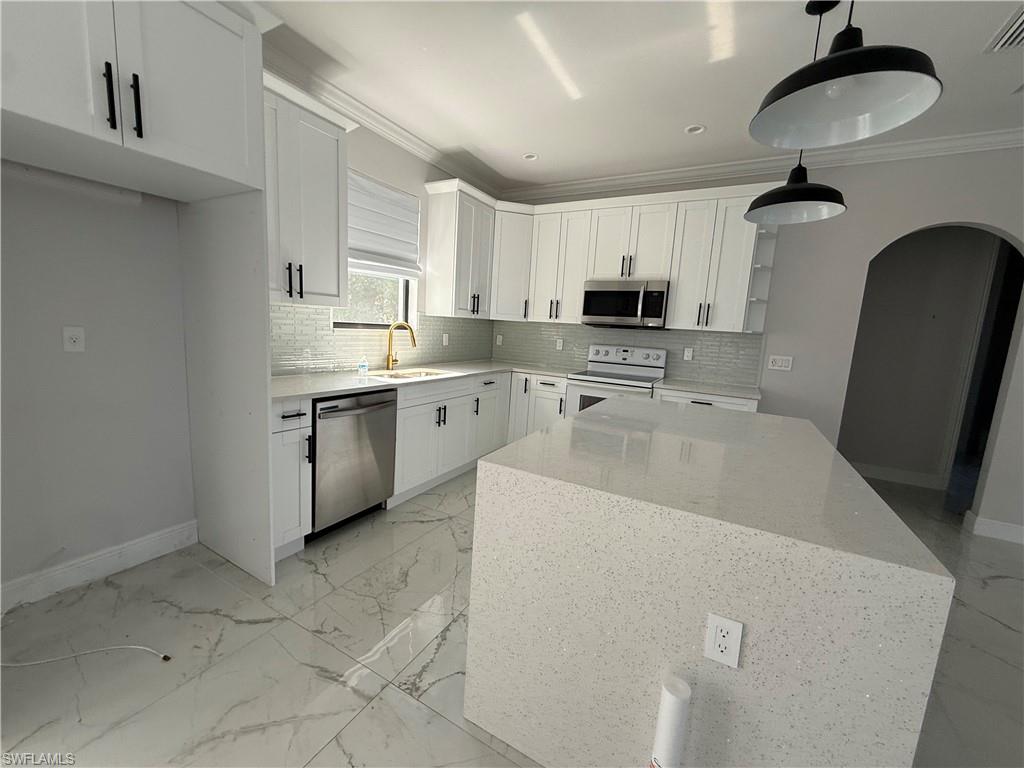 4768 40th Street Northeast Naples, FL 34120 - Photo 6 of 18 Modern kitchen featuring white shaker cabinetry, stainless steel appliances, a white tile backsplash, a large kitchen island with a light-colored countertop, and two pendant light fixtures