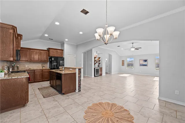 a large kitchen with kitchen island stainless steel appliances granite countertop a stove top oven a sink a counter top space cabinets and flat screen