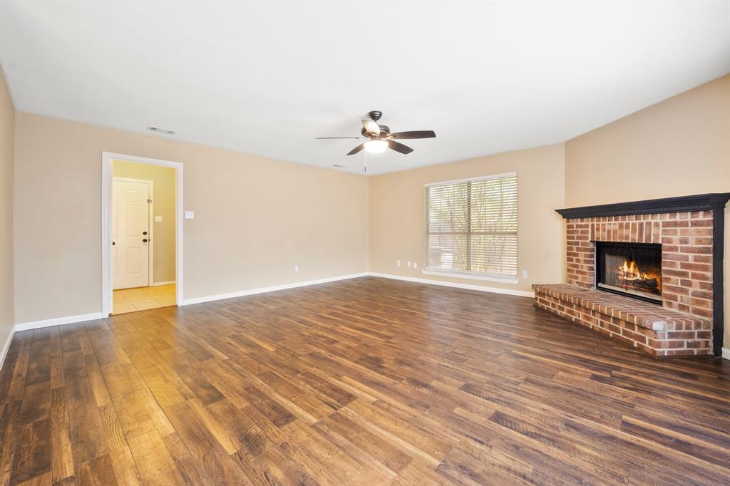 7517 Point Reyes Drive Fort Worth, TX 76137 - Photo 7 of 30 Spacious living area featuring wood-finish flooring, a brick fireplace with a dark wood mantel, and a large window with horizontal blinds