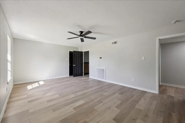 a view of an empty room with wooden floor and a ceiling fan