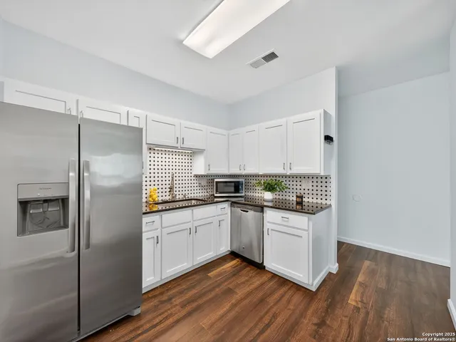 a kitchen with stainless steel appliances granite countertop a refrigerator a sink dishwasher a stove and white countertops with wooden floor