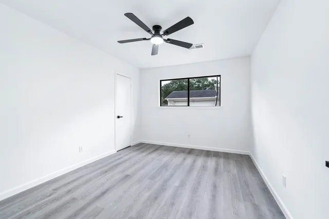 an empty room with wooden floor ceiling fan and windows