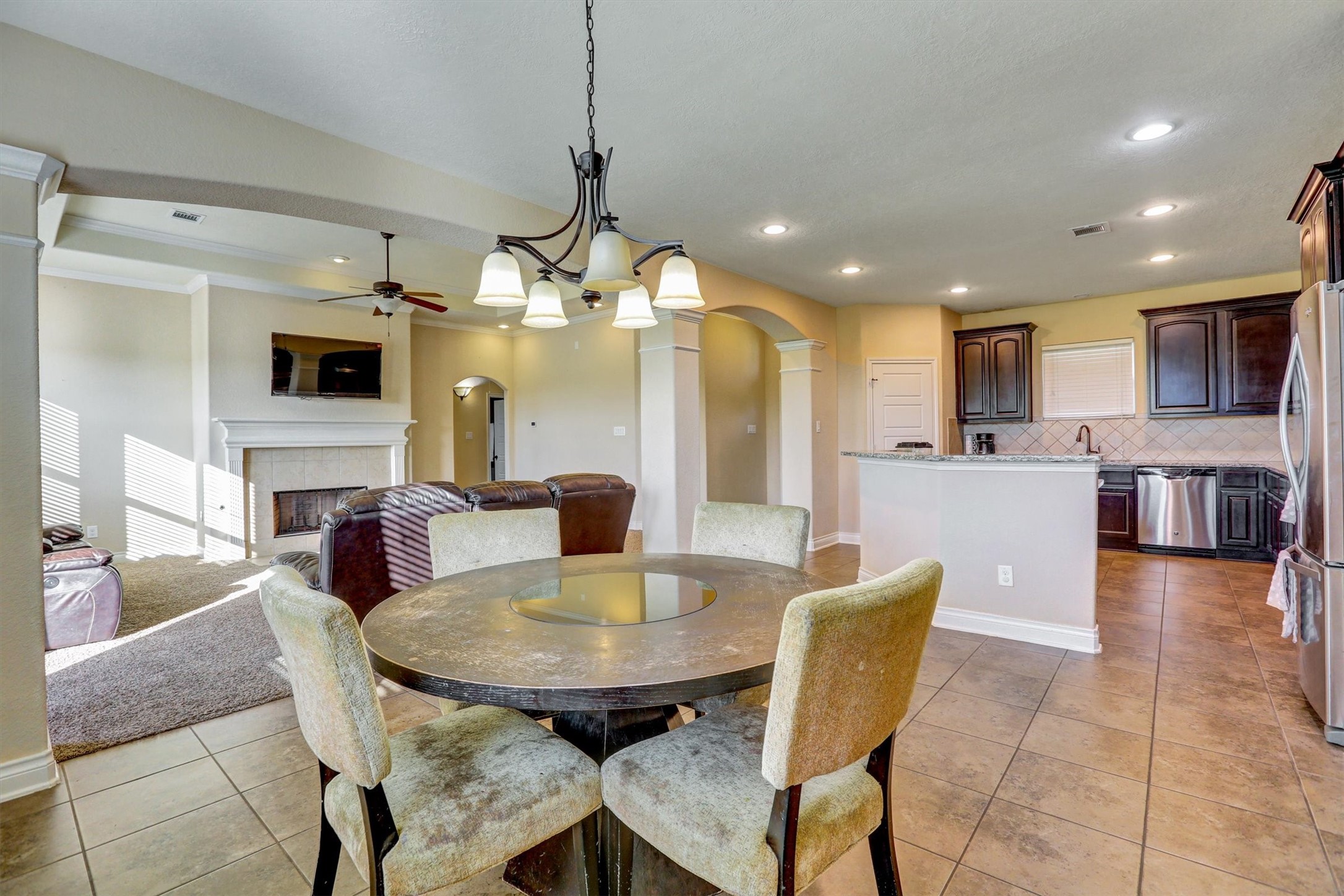 8131 Brinkmeyer Road Needville, TX 77461 - Photo 32 of 49 Open-concept living area featuring a cozy fireplace, elegant dining space, and a modern kitchen with dark wood cabinetry and stainless steel appliances.