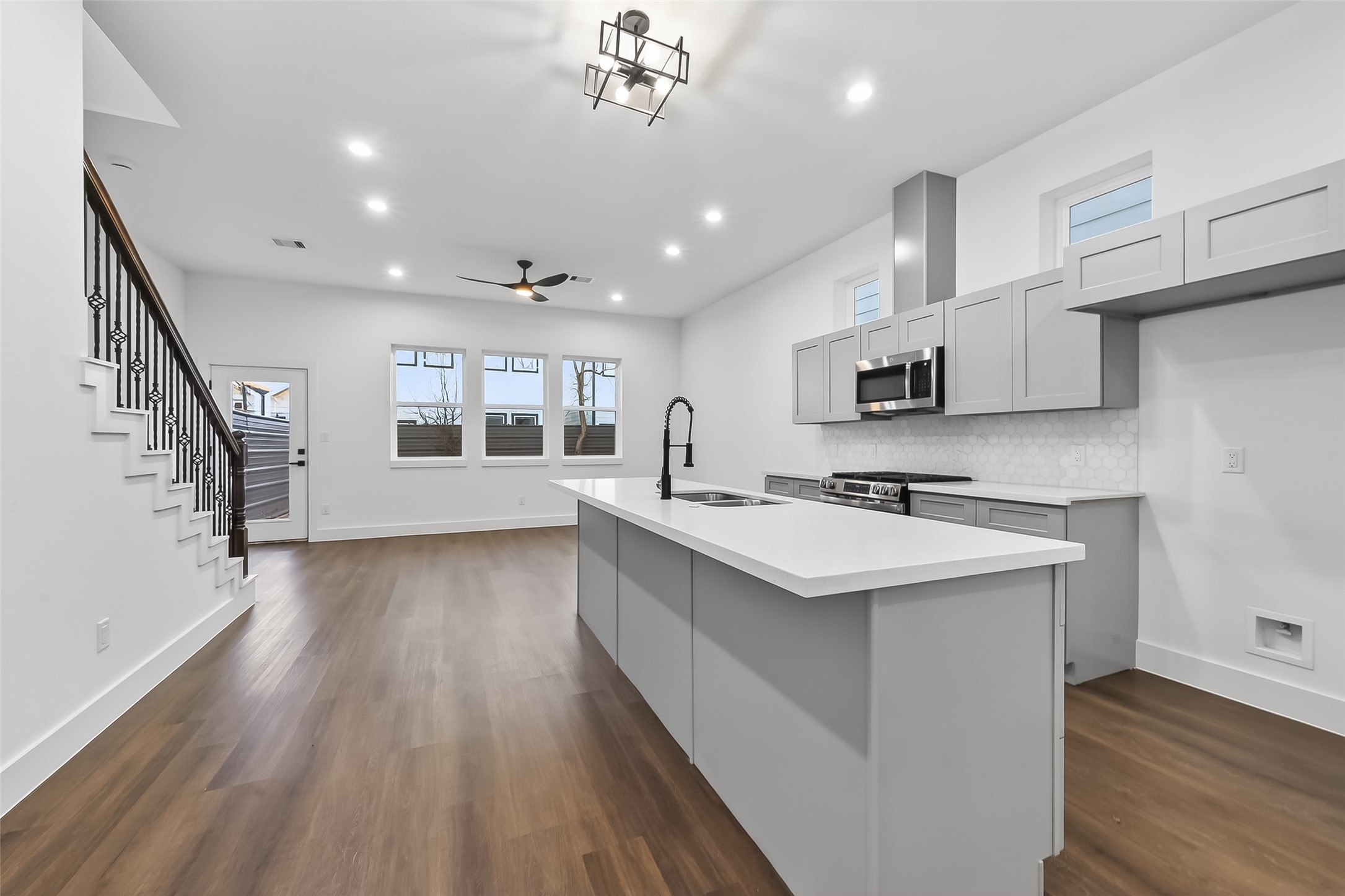 3514 Good Hope Street, Unit B Houston, TX 77021 - Photo 4 of 26 Modern open-concept kitchen and living area with sleek gray cabinetry, a large island, and hardwood floors. Features recessed lighting, stainless steel appliances, and a ceiling fan. Adjacent to a staircase and has ample natural light from large windows.