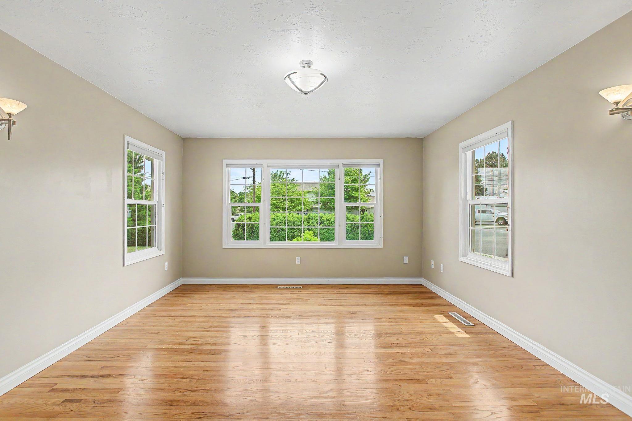 3314 6th Street Lewiston, ID 83501 - Photo 8 of 50 Spacious room featuring wood-finish flooring, light-toned walls, multiple windows, a ceiling-mounted light fixture, and two wall sconces