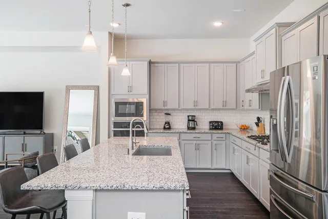 a kitchen with granite countertop a refrigerator oven a sink dishwasher and white cabinets with wooden floor