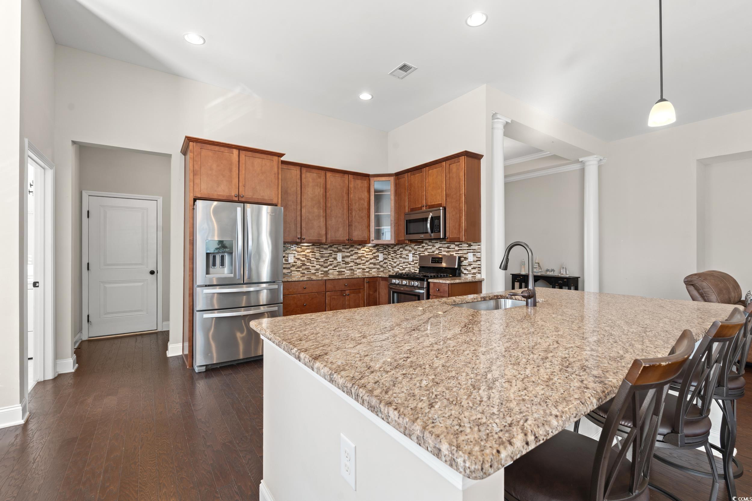 126 Viareggio Road Myrtle Beach, SC 29579 - Photo 7 of 40 Kitchen featuring brown cabinetry, stainless steel appliances, tasteful backsplash, hanging light fixtures, and glass insert cabinets