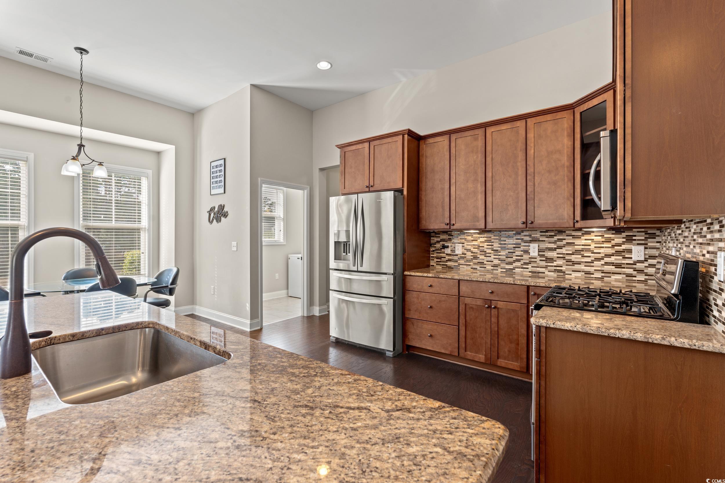 126 Viareggio Road Myrtle Beach, SC 29579 - Photo 8 of 40 Kitchen featuring appliances with stainless steel finishes, light stone countertops, pendant lighting, dark wood-style flooring, and backsplash