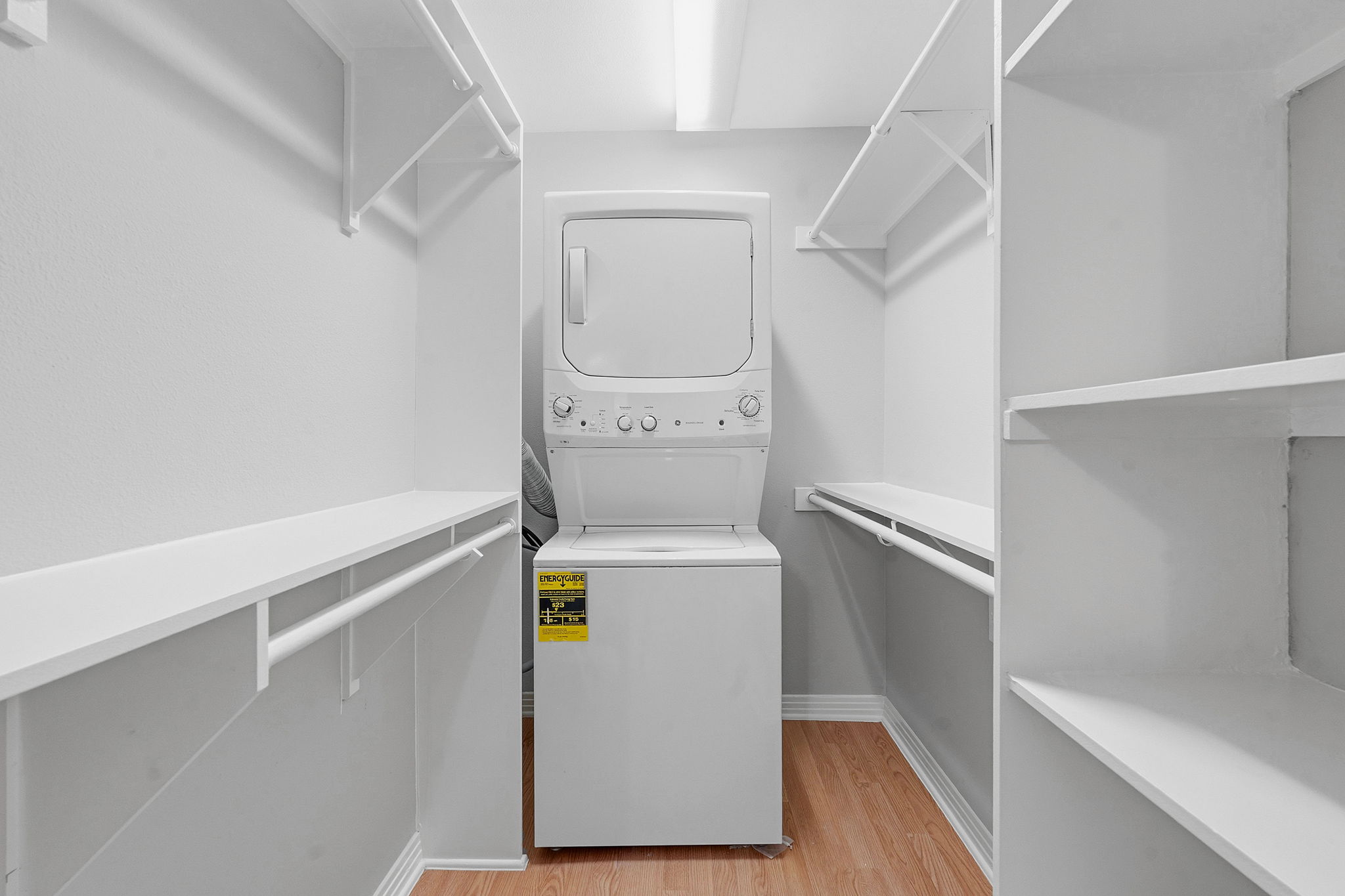 1422 Collier Street, Unit 203 Austin, TX 78704 - Photo 17 of 21 Convenient laundry area featuring a stacked washer and dryer unit, integrated into a closet with ample shelving and hanging rods, set on wood-look flooring