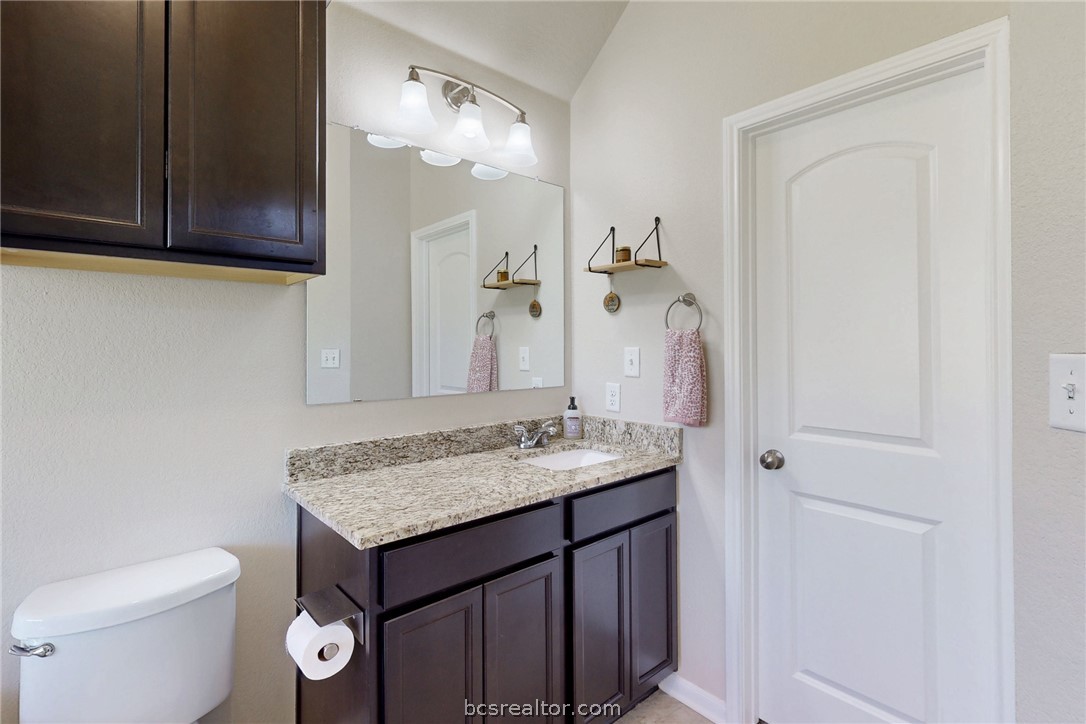 2071 Positano Loop Bryan, TX 77808 - Photo 16 of 31 a bathroom with a granite countertop sink a toilet and a mirror