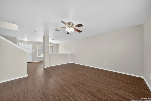 an empty room with wooden floor chandelier fan and windows