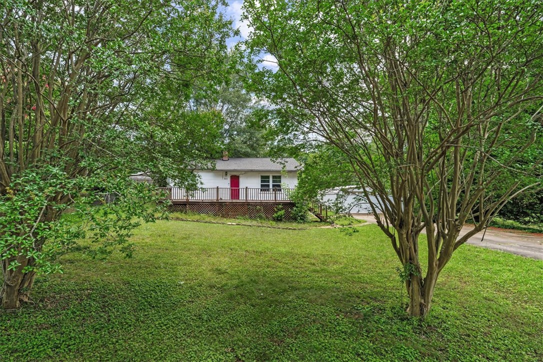 208 Holleman Street Seneca, SC 29678 - Photo 3 of 27 This charming residence features a classic white facade and a welcoming red door, nestled amidst lush greenery.