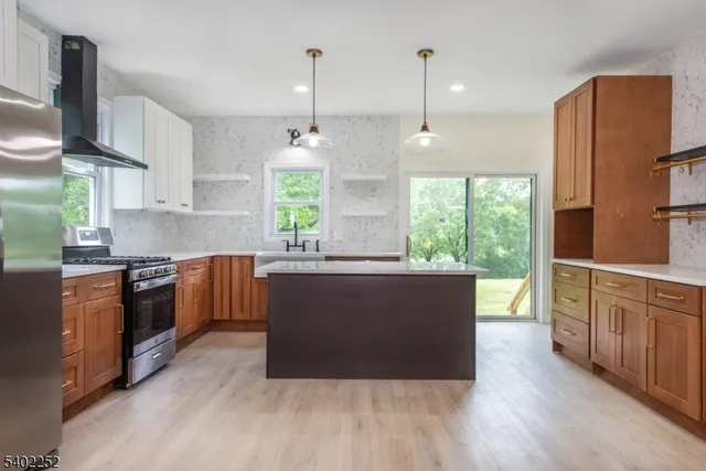 a kitchen with stainless steel appliances granite countertop a refrigerator a sink dishwasher a oven and a dining table with wooden floor