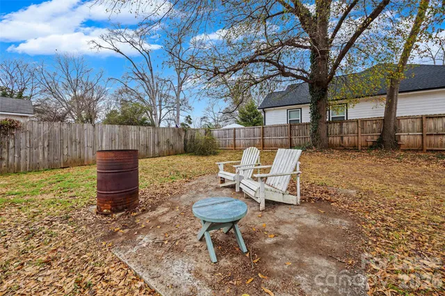 a view of a backyard with table and chairs potted plants and a large tree