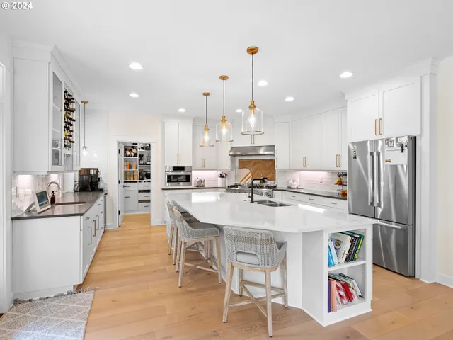 a kitchen with stainless steel appliances kitchen island granite countertop a refrigerator a stove a sink a dining table and chairs with wooden floor