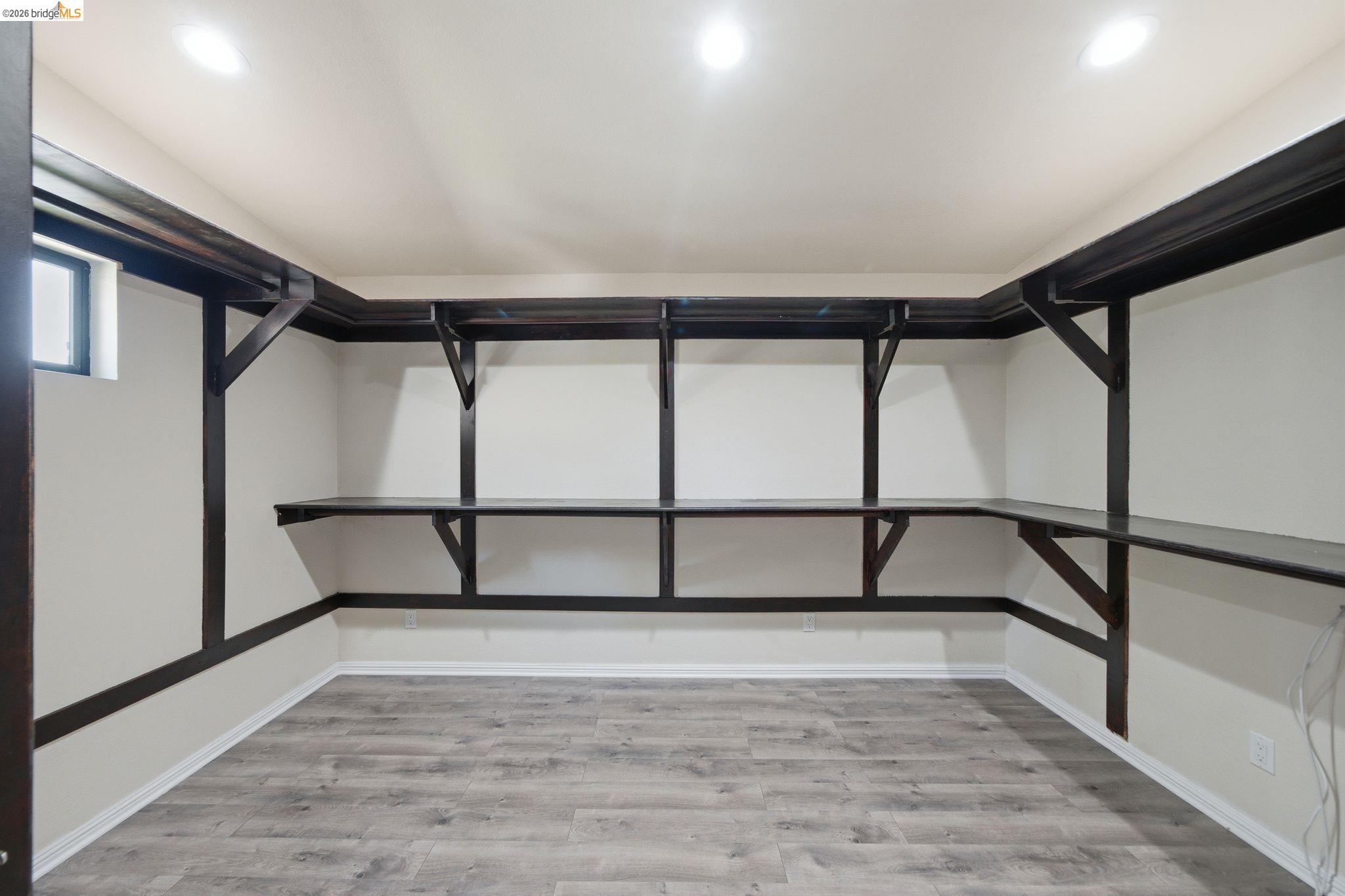11133 Golf Links Road Oakland, CA 94605 - Photo 33 of 57 Room featuring extensive built-in dark wood shelving and desk space, recessed ceiling lighting, light gray wood-finish flooring, white baseboards, and a small casement window
