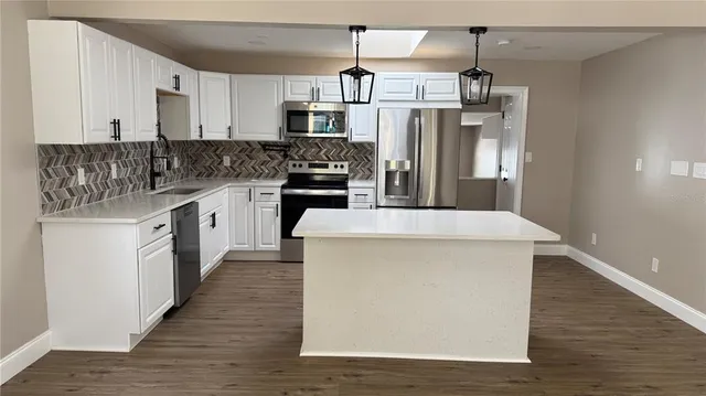 a kitchen with stainless steel appliances kitchen island granite countertop a refrigerator a stove a sink and white cabinets with wooden floor