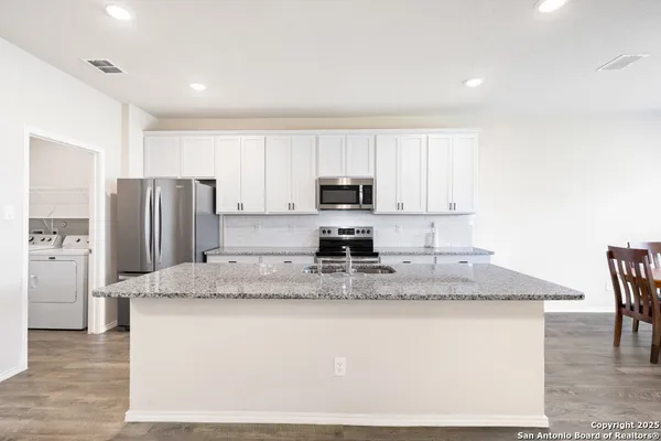 a kitchen with kitchen island granite countertop a stove a sink a refrigerator with white cabinets and wooden floor