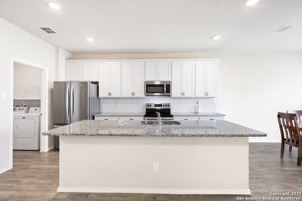 19916 Doc Holiday Drive Lytle, TX 78052 - Photo 7 of 27 a kitchen with kitchen island granite countertop a stove a sink a refrigerator with white cabinets and wooden floor