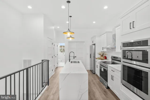 a kitchen with stainless steel appliances kitchen island granite countertop a stove a sink a refrigerator and white cabinets with wooden floor