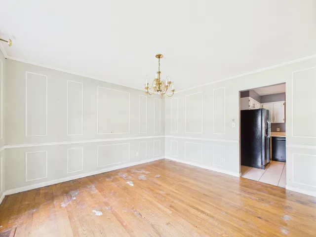 an empty room with wooden floor chandelier and windows