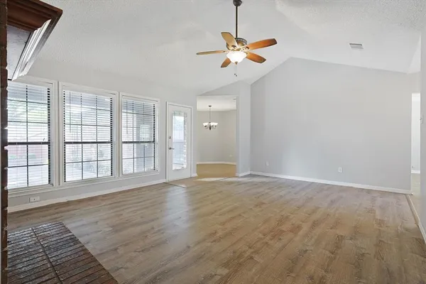 an empty room with wooden floor fan and windows