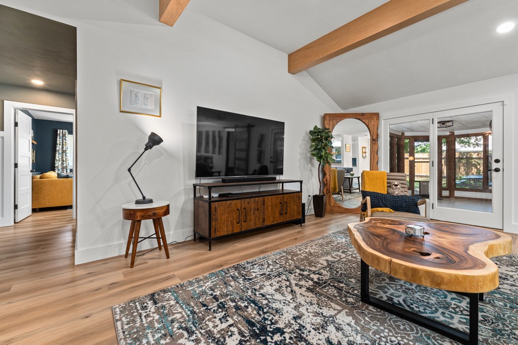 Exposed wood beams add architectural interest to this inviting living area, which features wide plank flooring and access to a bright outdoor space.