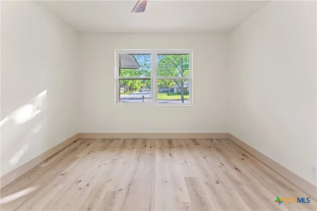 an empty room with wooden floor chandelier fan and windows