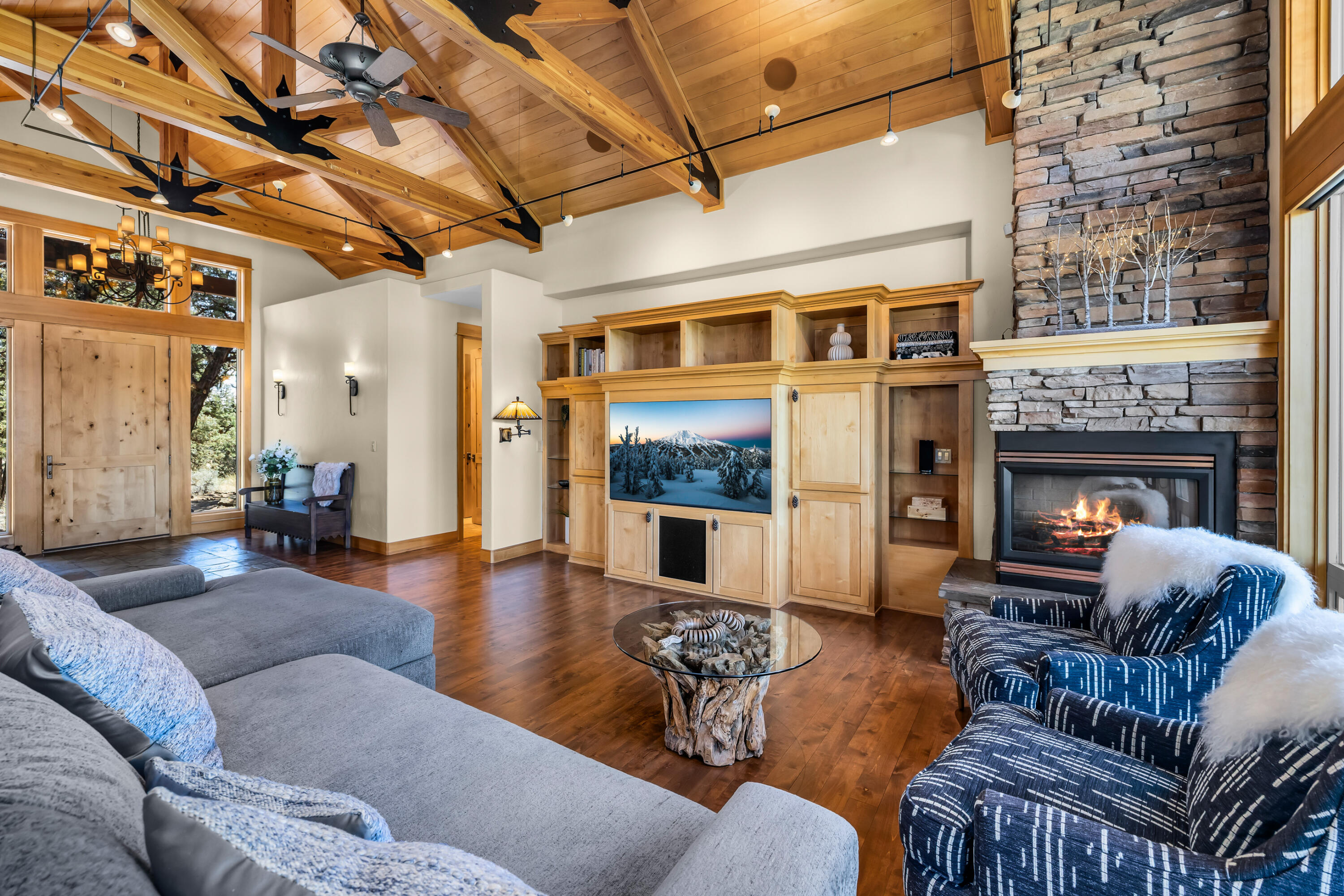 64145 Hunnell Road Bend, OR 97703 - Photo 10 of 65 The great room showcases PacWest craftsmanship with vaulted wood ceilings, exposed trusses, real wood floors and a dramatic stone fireplace, creating a warm gathering space designed around the Cascade Mountain views.
