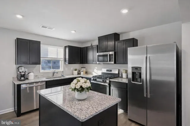 a kitchen with stainless steel appliances granite countertop a sink a stove a refrigerator a center island and cabinets