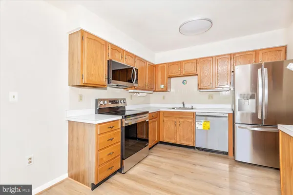 a view of an empty room with wooden floor and a kitchen