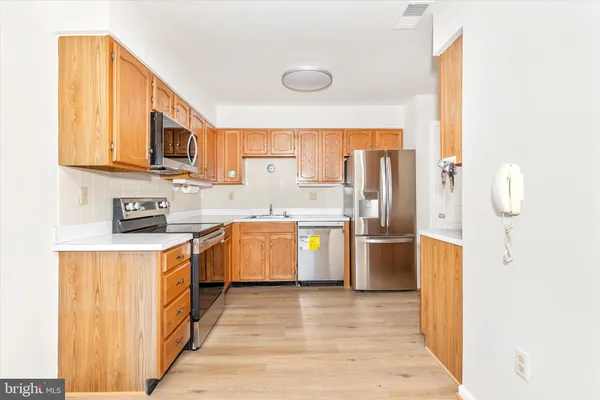 a view of an empty room with wooden floor and a kitchen