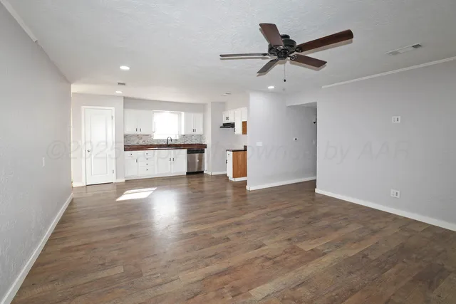 a view of an empty room with kitchen and window