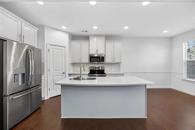 a view of an empty room with wooden floor a ceiling fan and kitchen view