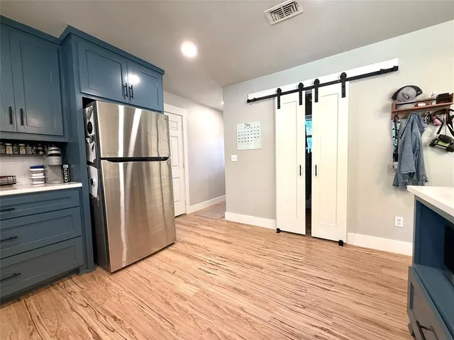a view of a refrigerator in kitchen and an empty room with wooden floor