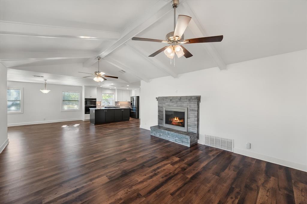 917 Goodwyn Road Italy, TX 76651 - Photo 13 of 40 Vaulted ceilings with exposed beams, wood-finish flooring, stone-clad fireplace, ceiling fans, and an open concept layout