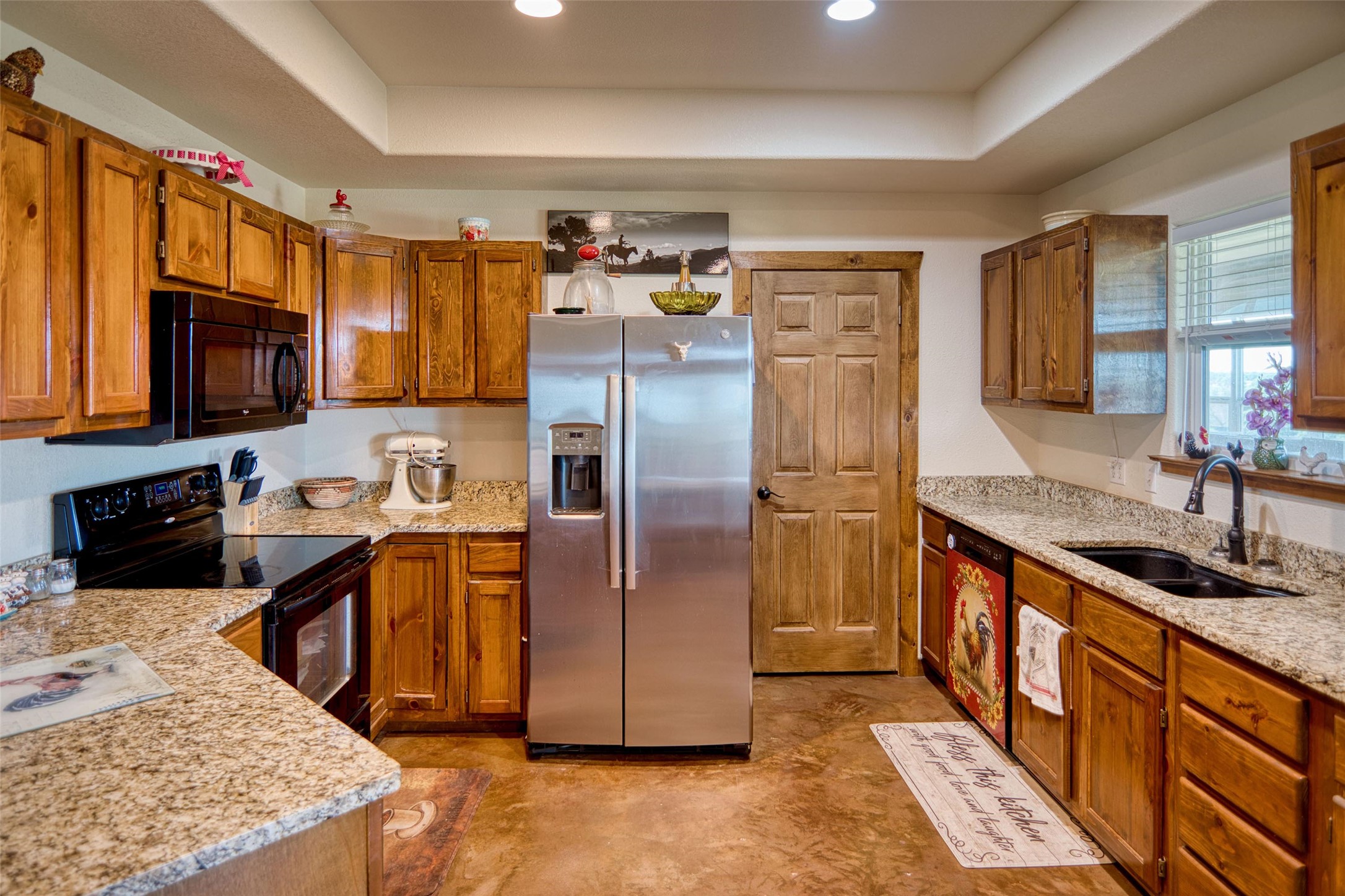 12119 Highway 29 Llano, TX 78643 - Photo 5 of 40 Kitchen featuring black appliances, a tray ceiling, brown cabinetry, light stone counters, and recessed lighting