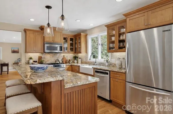 a kitchen with stainless steel appliances granite countertop a refrigerator a sink dishwasher a stove and white countertops with wooden floor