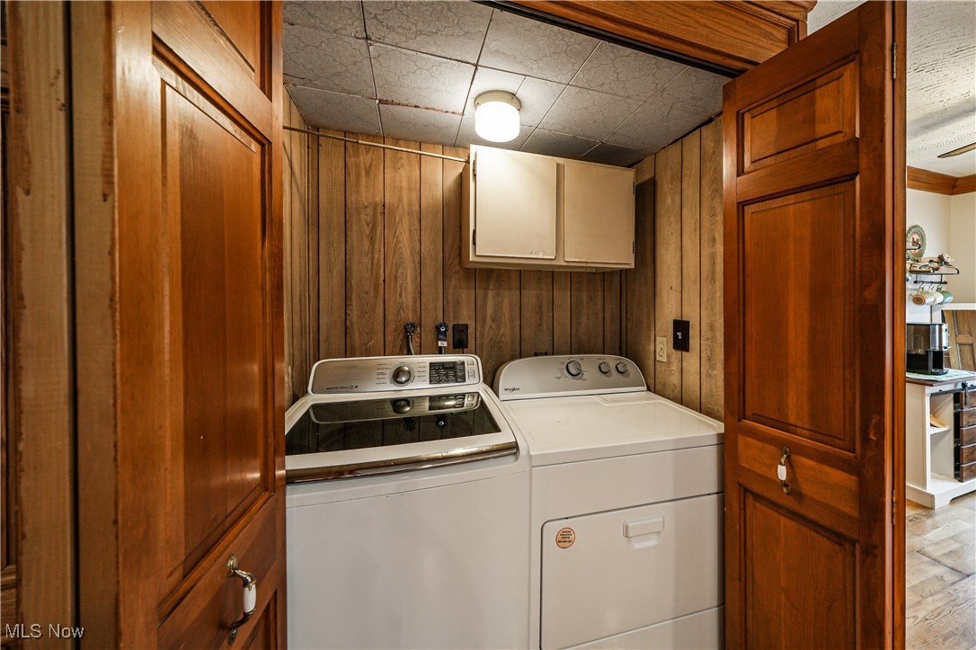 4819 Westbourne Road Cleveland, OH 44124 - Photo 33 of 39 Laundry room with wooden walls, washer and dryer, light wood-style flooring, and cabinet space