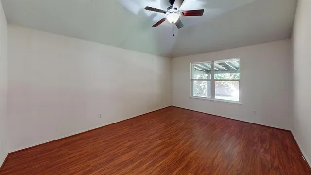 an empty room with wooden floor chandelier fan and windows