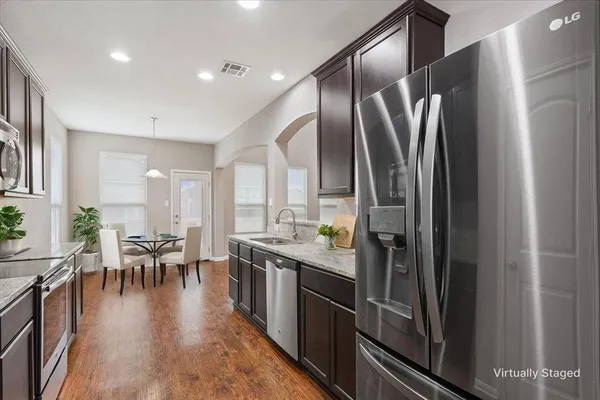 a kitchen with stainless steel appliances granite countertop a refrigerator a stove and a dining table with wooden floor