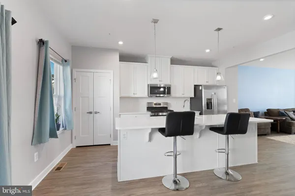 a kitchen with stainless steel appliances kitchen island granite countertop a refrigerator a stove a dining table and chairs with wooden floor